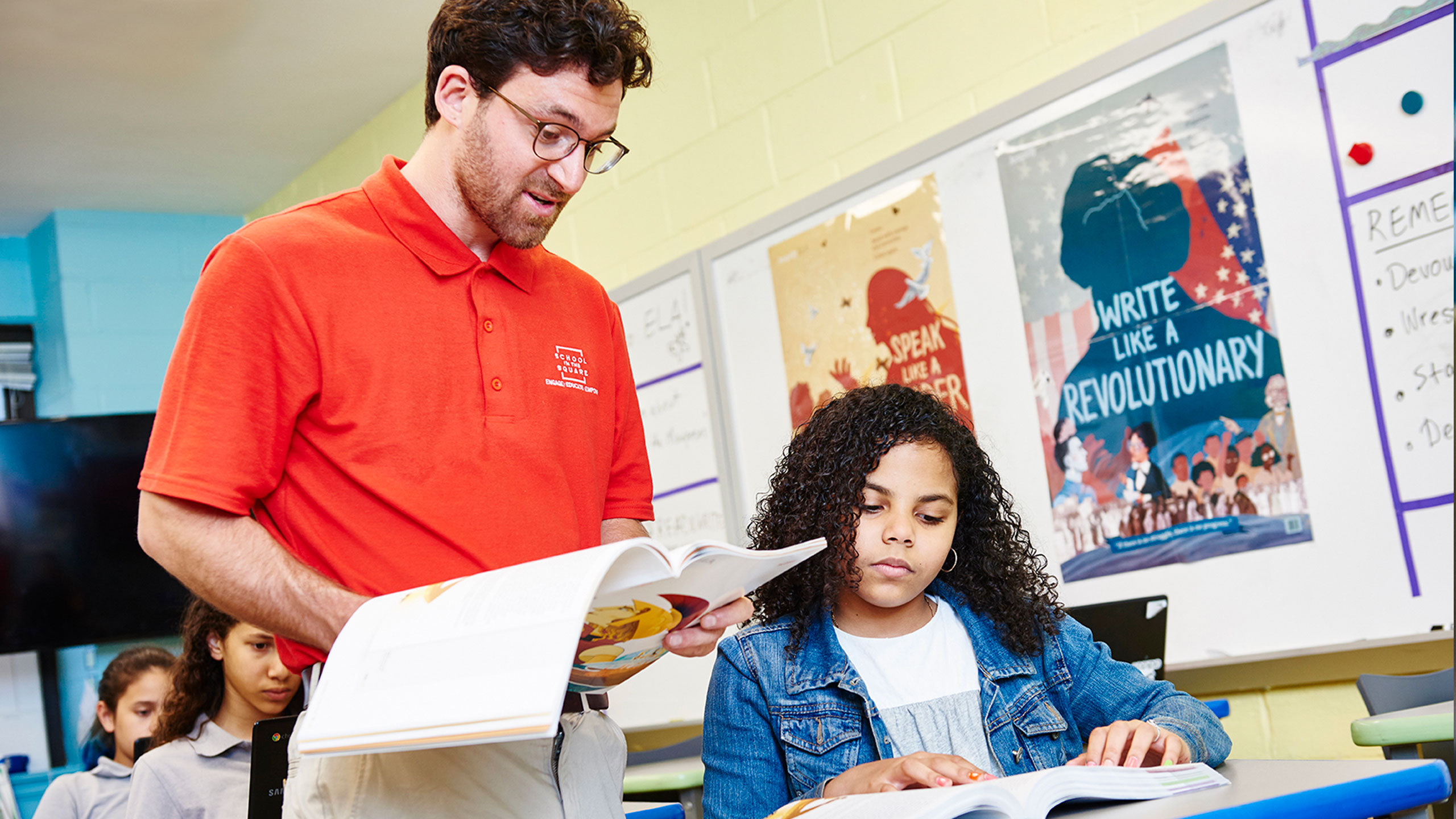 Teacher standing over a student reading to her