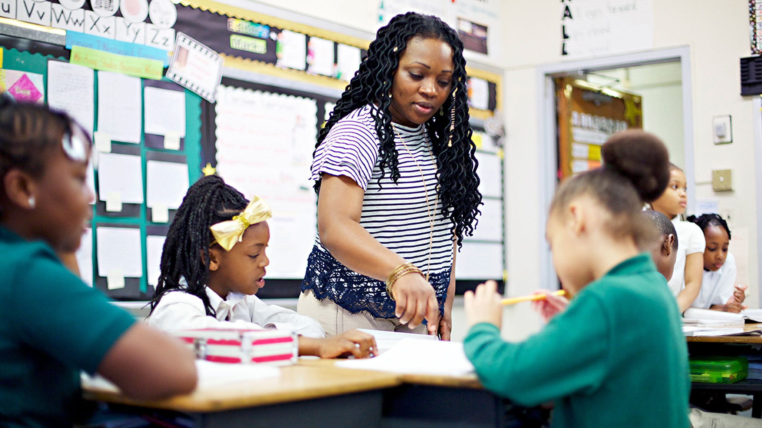 Three children seated while the teacher points out something in a book